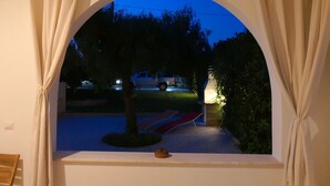 A view through an arched window with curtains, revealing a driveway, a tree, and a vehicle in the background. - Blue House Torre Pali Pescoluse (SALVE)