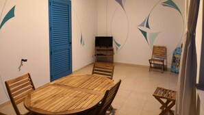 A room with a wooden dining table, four chairs, a television on a stand, a blue door, and abstract wall art. - Blue House Torre Pali Pescoluse (SALVE)