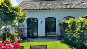 Una casa con tetto in tegole, un portone d'ingresso e un piccolo giardino con una panchina e un tavolo.