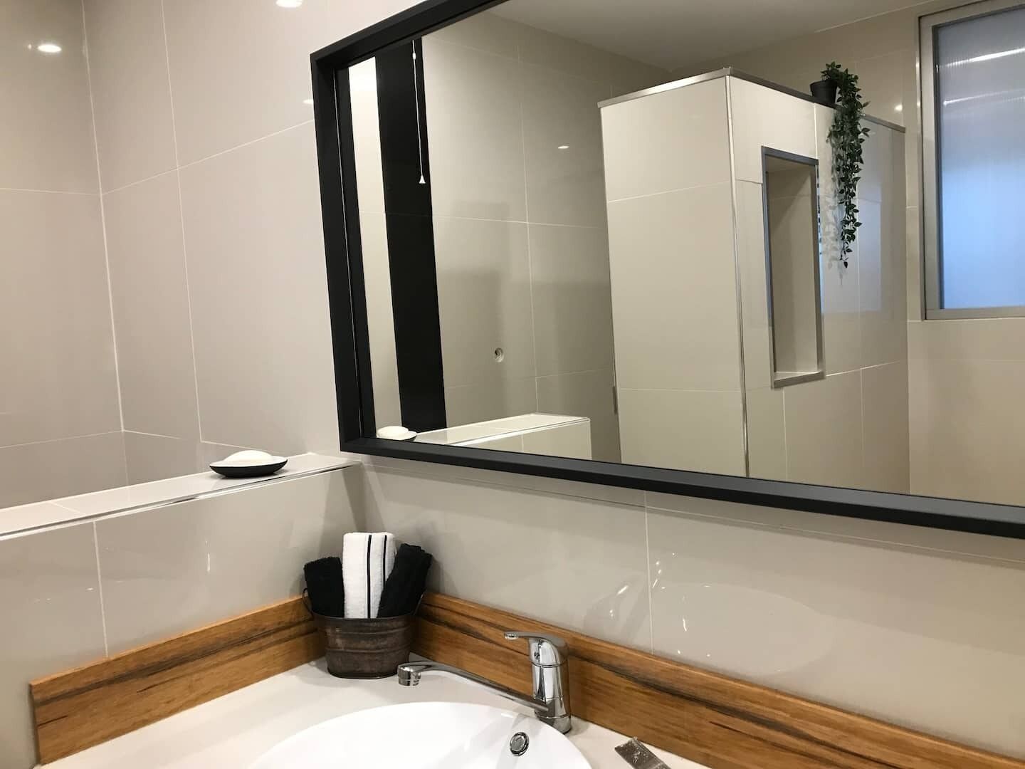 A modern bathroom with a large mirror, a sink with a wooden countertop, and a towel holder.