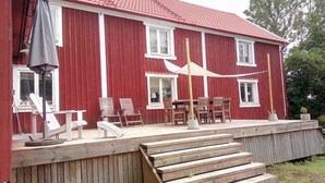 Ein rotes Holzgebäude mit überdachter Außenbestuhlung, inklusive Stühle und Tisch.