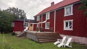 Een rode houten woning met een veranda, buitenmeubels en een kleine schuur.