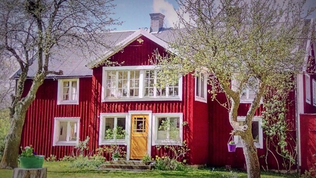 Ein zweistöckiges rotes Haus mit Holztür, Fenstern mit weißen Rahmen und einem geneigten Dach.