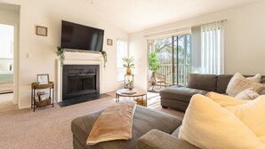 Ein Wohnzimmer mit Kamin, Flachbildfernseher, Sofa und Balkon mit Stuhl.