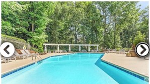 Ein Swimmingpool mit Liegestühlen und einer Pergola, umgeben von Bäumen.