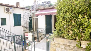 Edifício residencial com escadaria, portão e parede de pedra com vegetação.