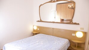 Quarto com cama, um espelho grande e duas luminárias de cabeceira.