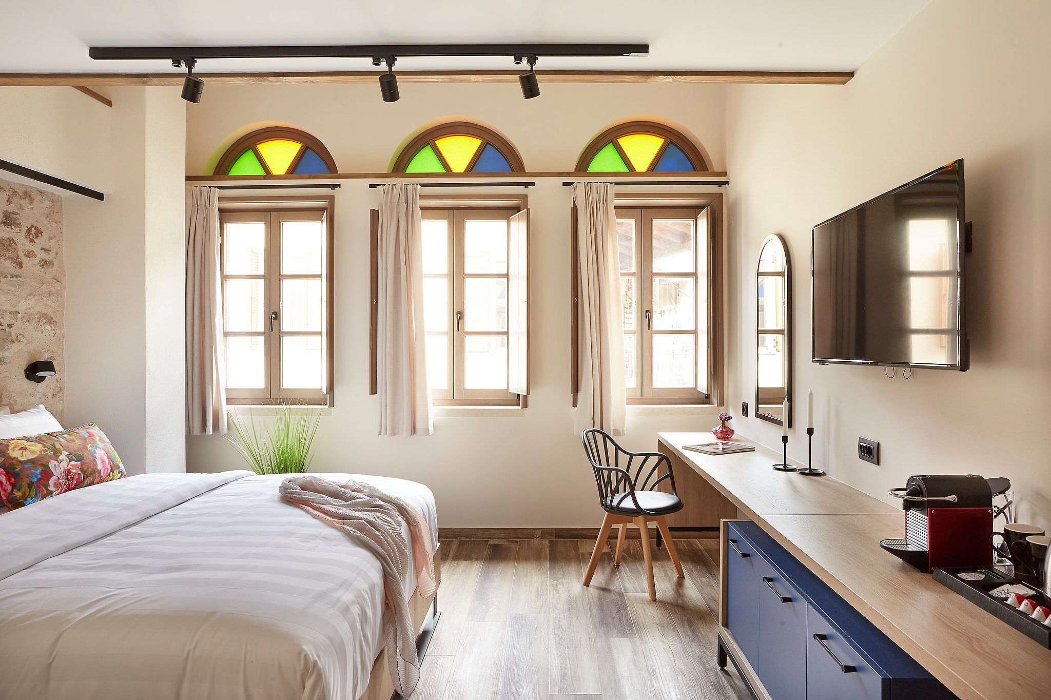 A bedroom with a bed, a desk, a chair, a TV, and a coffee machine.