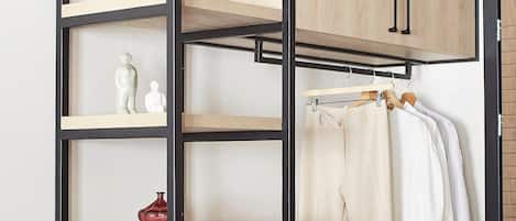 Una habitación pequeña con un escritorio de madera, un estante colgante con objetos decorativos, un perchero con ropa, un bolso de mano y un par de zapatos.