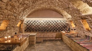 Una cava de vinos con paredes de piedra, una estantería para botellas y una mesa con botellas y copas.
