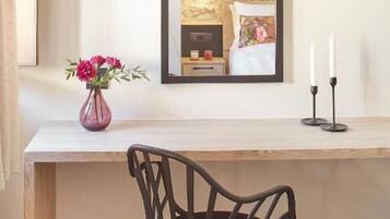 A wooden desk with a black chair, a vase of flowers, and a mirror on the wall.