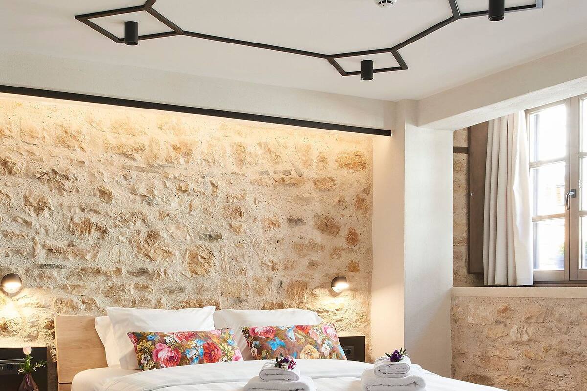 Un dormitorio moderno con cama de madera, pared de piedra y diseño geométrico en el techo.