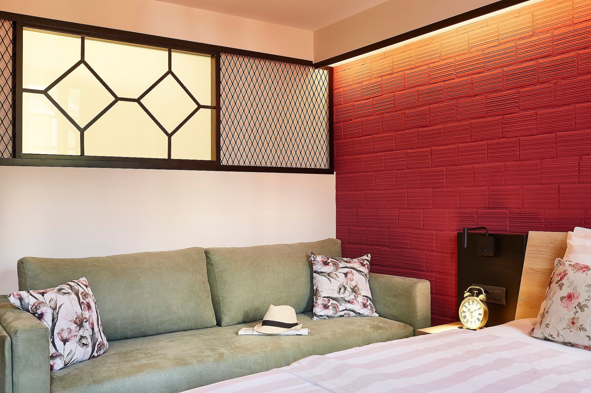 Ein Zimmer mit einem grünen Sofa, floralen Kissen, einem Hut und einem Nachttisch mit Lampe und Wecker.
