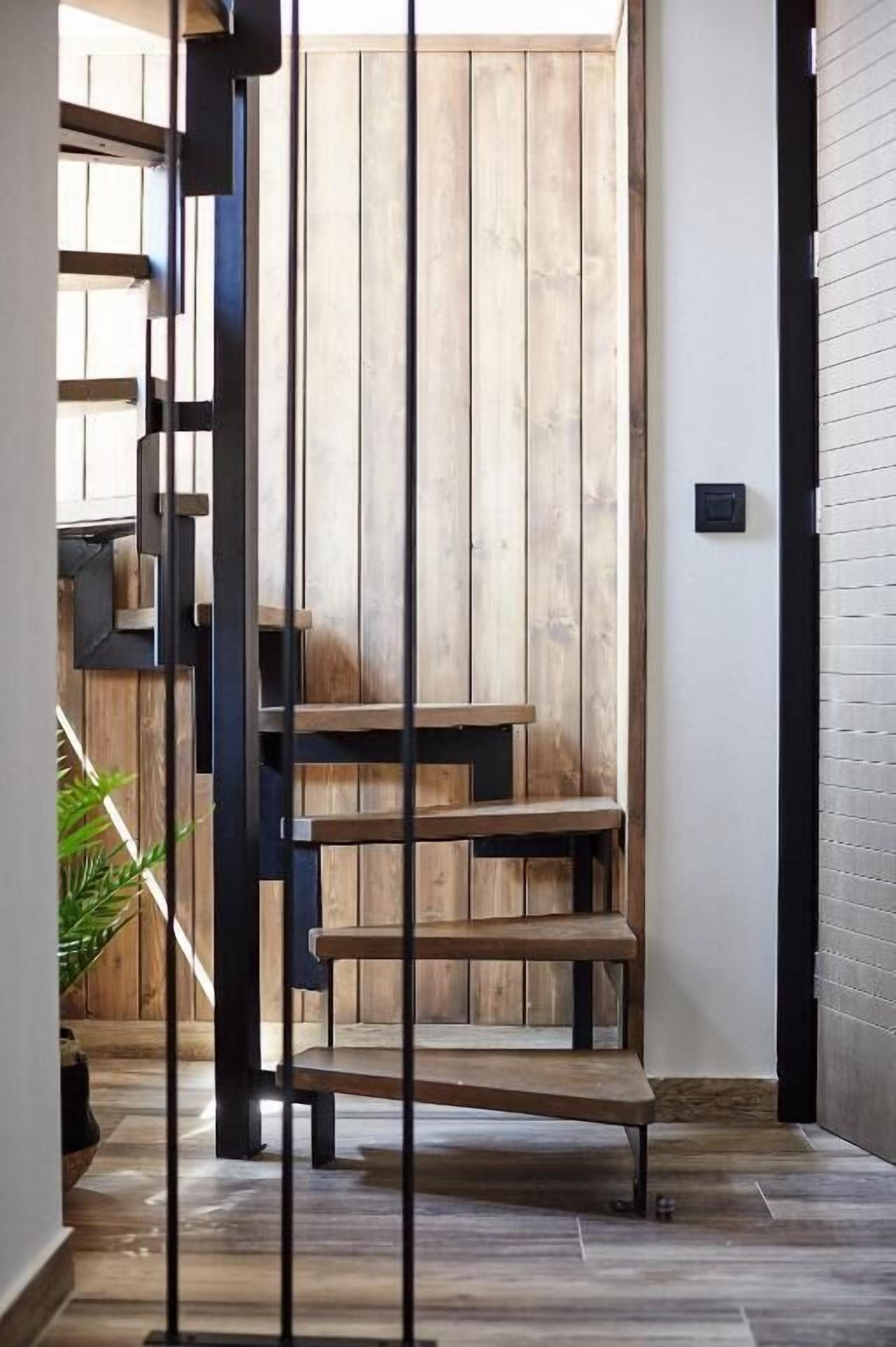 Una escalera de madera con peldaños de madera y barandillas de metal negro que lleva a una puerta de madera.
