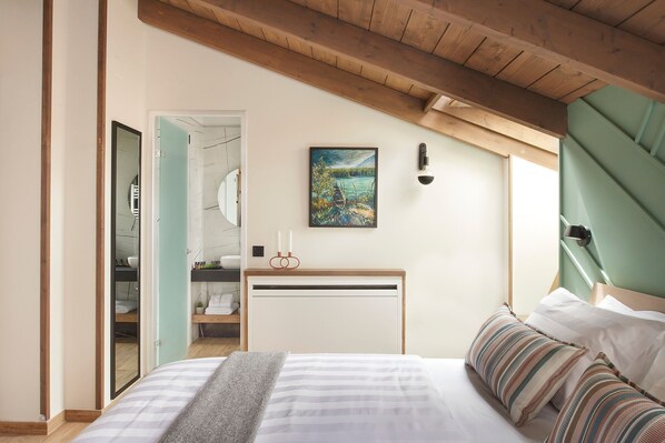 A bedroom with a bed, a bedside table, a painting, and a view of a bathroom.