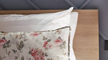 Una cama con almohada estampada y cabecera de madera, sobre un fondo gris.