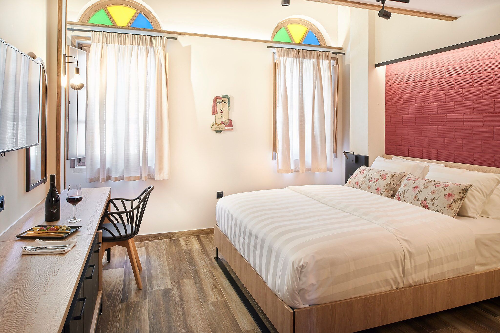 A bedroom with a wooden bed, a desk with a bottle and glasses, and a chair.