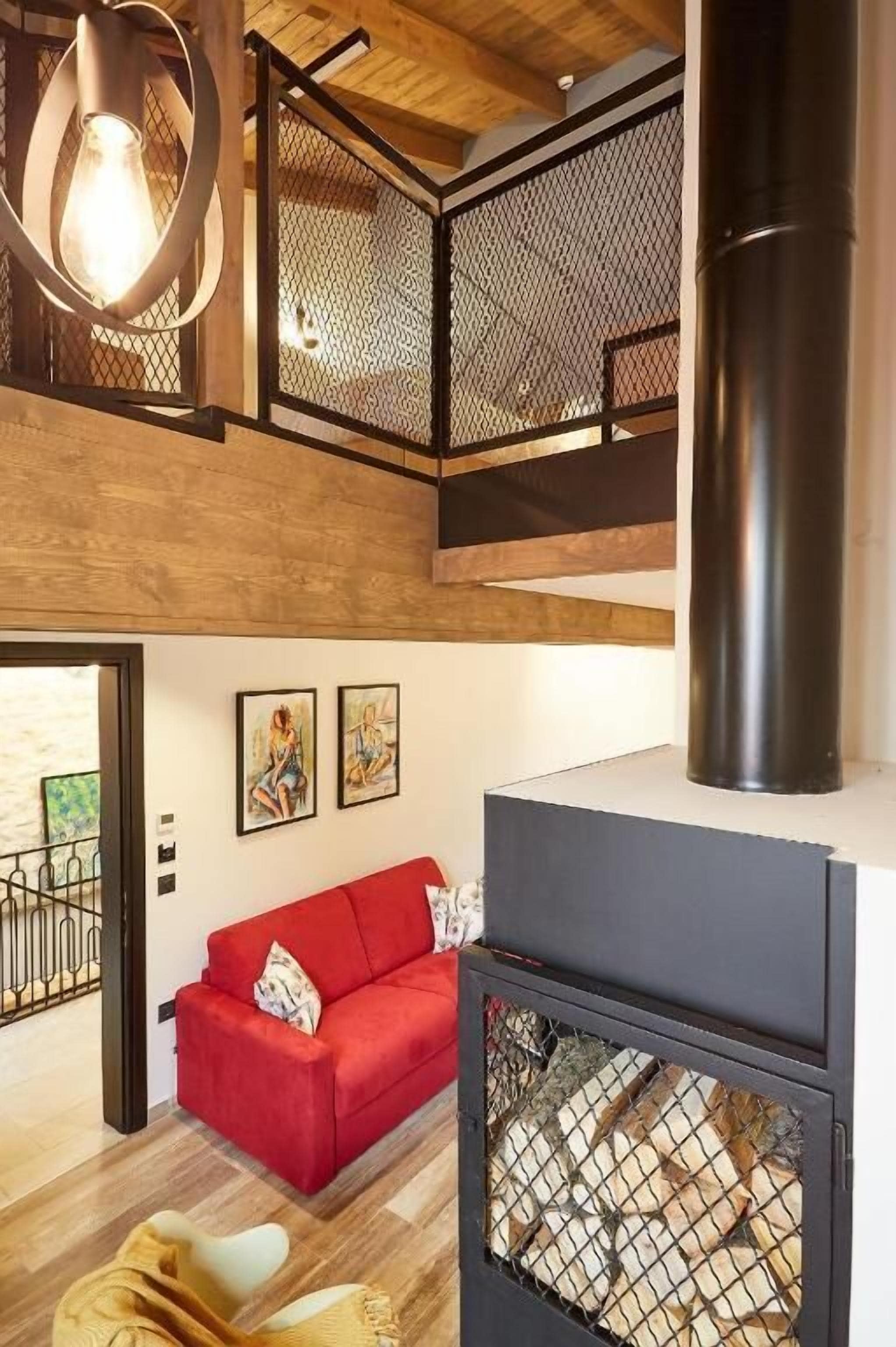 Un interior moderno con un sofá rojo, suelo de madera, chimenea negra y una lámpara colgante.