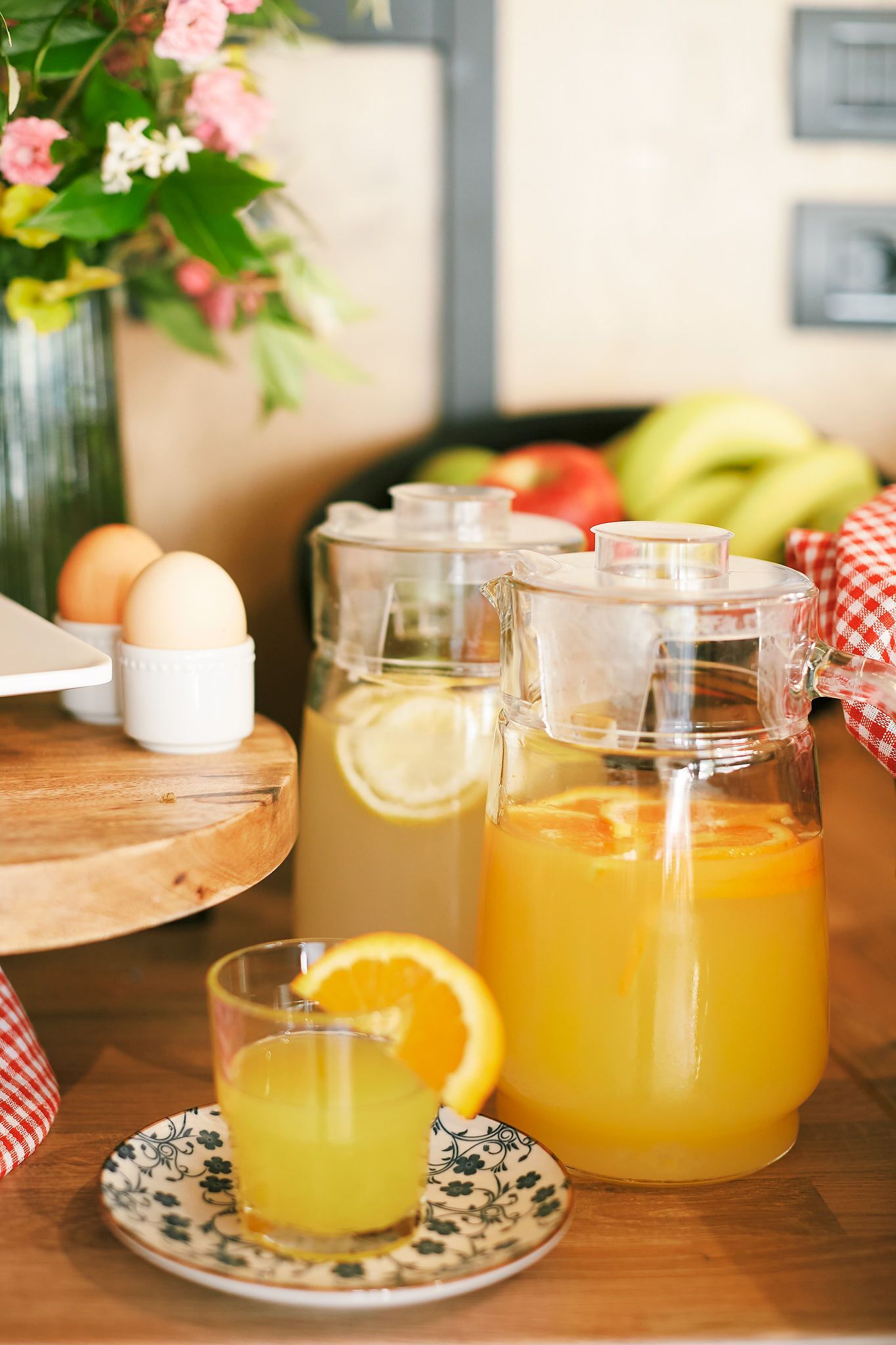 A breakfast setting with a pitcher of orange juice, a glass of orange juice, eggs, and a vase of flowers.