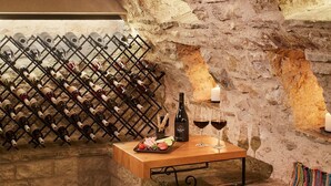 Una cava de vinos con una estantería, una mesa de madera con botellas de vino, copas y una vela.