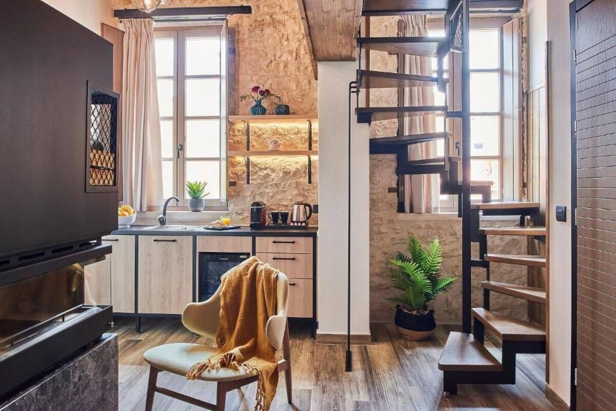 Una cocina compacta con horno empotrado, un comedor con una silla y una escalera que sube a un nivel superior.