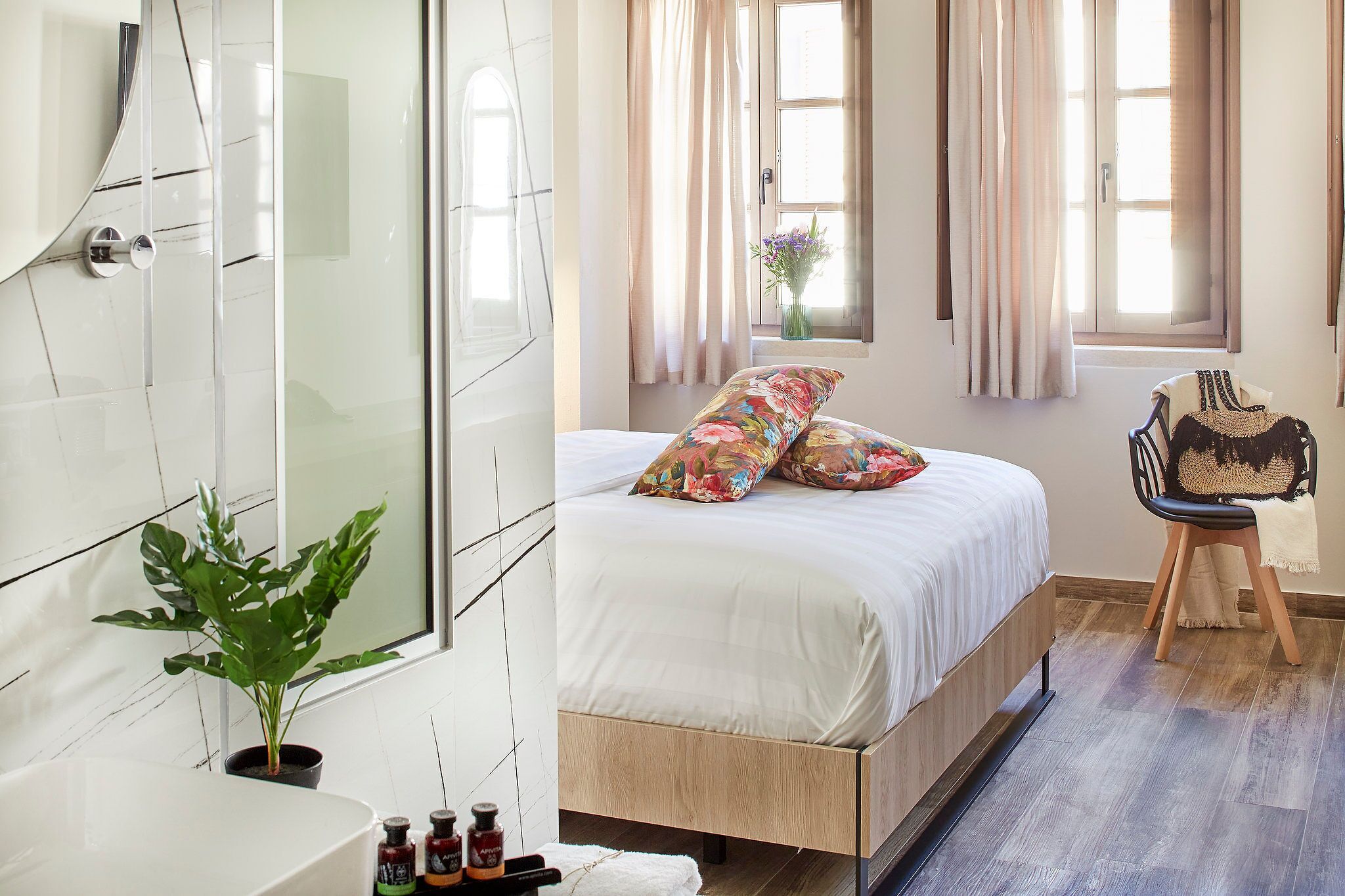 A bedroom with a bed, a potted plant, a chair, and a window with curtains.