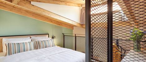 Una camera da letto con un letto, travi a vista in legno, una finestra e un balcone con ringhiera in metallo.