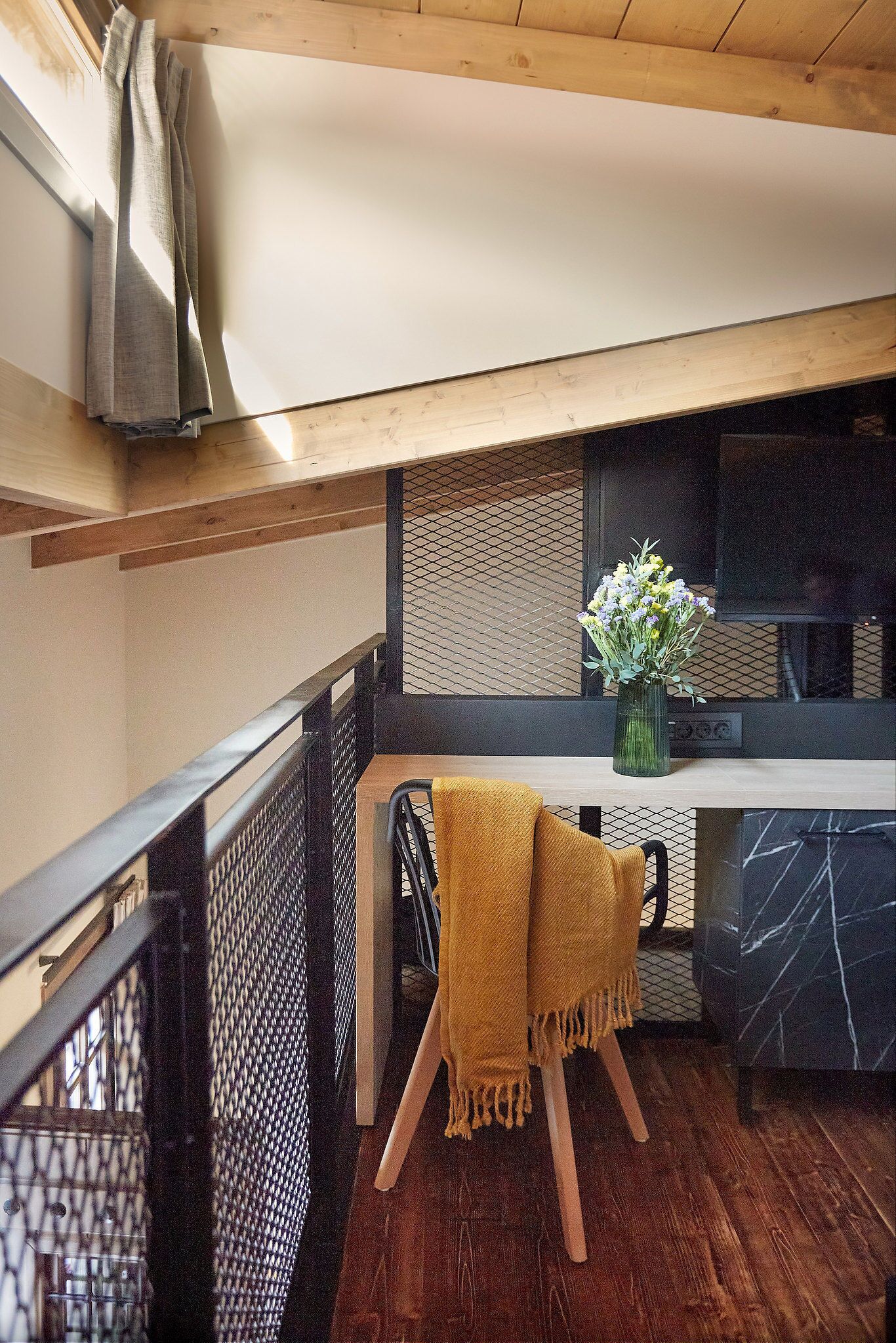 A modern room with a wooden ceiling, a black mesh partition, a wooden table with a yellow throw, and a vase with flowers.