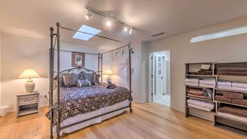 A four-poster bed with a patterned bedspread, bedside lamps, and a wooden floor.