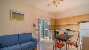 A living room with a blue sofa, a dining table with chairs, and a kitchen area with wooden cabinets and a refrigerator. - LA TERRAZZA A SECCHETO SUL MARE (Campo nell'Elba)