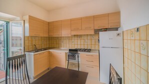 A compact kitchen with wooden cabinets, a gas stove, a white refrigerator, and a dining table. - LA TERRAZZA A SECCHETO SUL MARE (Campo nell'Elba)