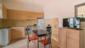 A compact kitchen with wooden cabinets, a dining table with two chairs, a built-in oven, and a TV on a cabinet. - LA TERRAZZA A SECCHETO SUL MARE (Campo nell'Elba)