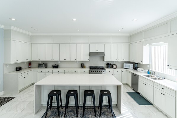 A modern kitchen with white cabinetry, a central island with stools, and built-in appliances. - Huge Family Home Near Disneyland & SoCal Beaches (Midway City)
