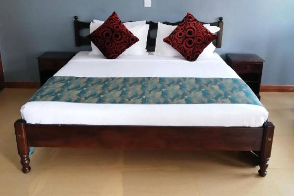 A bed with a patterned bedspread, two decorative pillows, a wooden headboard, and two bedside tables.