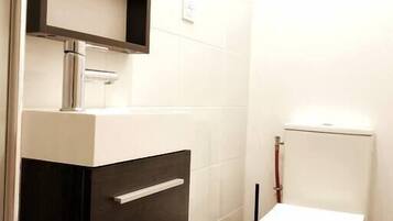 Une petite salle de bain avec des toilettes blanches, un lavabo de couleur foncée et un miroir au-dessus du lavabo.