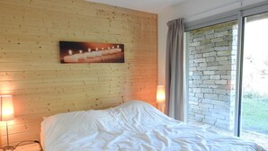 Ett sovrum med en väggpanel av trä, en säng med vita sängkläder, två sänglampor och ett fönster med en vägg av sten.