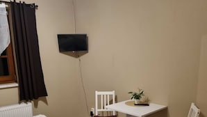 A small, tidy room with a bed, a chair, a small table, and a TV mounted on the wall.