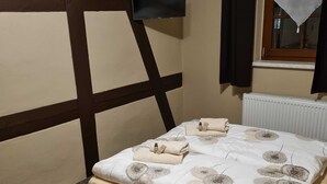 Un dormitori amb un llit, una televisió penjada a la paret, una finestra amb cortines i un radiador.