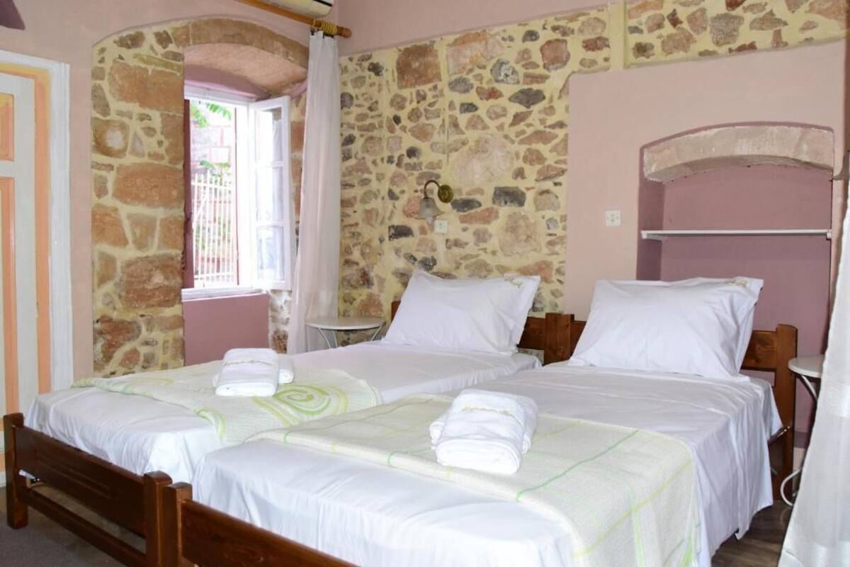 A room with two beds, stone walls, and a window with curtains.