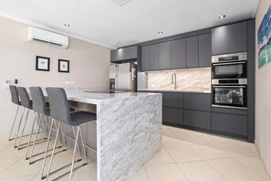 A modern kitchen with dark cabinets, a marble island, and a built-in oven. - Den Laman Tuna directly on the sea with amazing views (Kralendijk)