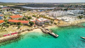 Una vista aerea di una cittadina costiera con un molo che si protende in acque color turchese, circondata da edifici e da una spiaggia.
