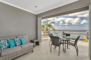 En balkon med sofa og spisebord, med udsigt over en strand og hav.
