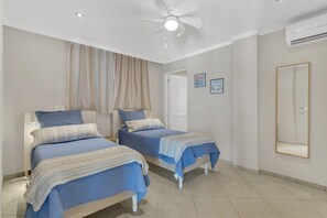 A bedroom with two beds, a ceiling fan, a door, and a wall-mounted mirror.