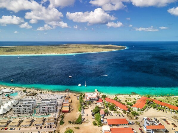An aerial view of a coastal resort with multiple buildings, a marina, and a clear view of the ocean and distant islands.
