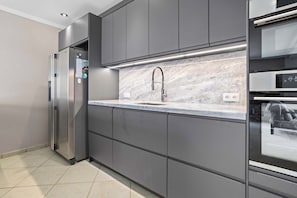 A modern kitchen with grey cabinets, a stainless steel refrigerator, a marble countertop, and a built-in oven. - Den Laman Tuna directly on the sea with amazing views (Kralendijk)