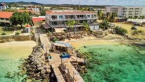 Un hotel sul lungomare con un molo, acque turchesi cristalline e vista sul paesaggio circostante.