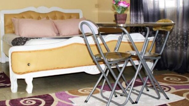 Una stanza con un letto, un tavolo con sedie, una pianta in vaso e una finestra con tende.