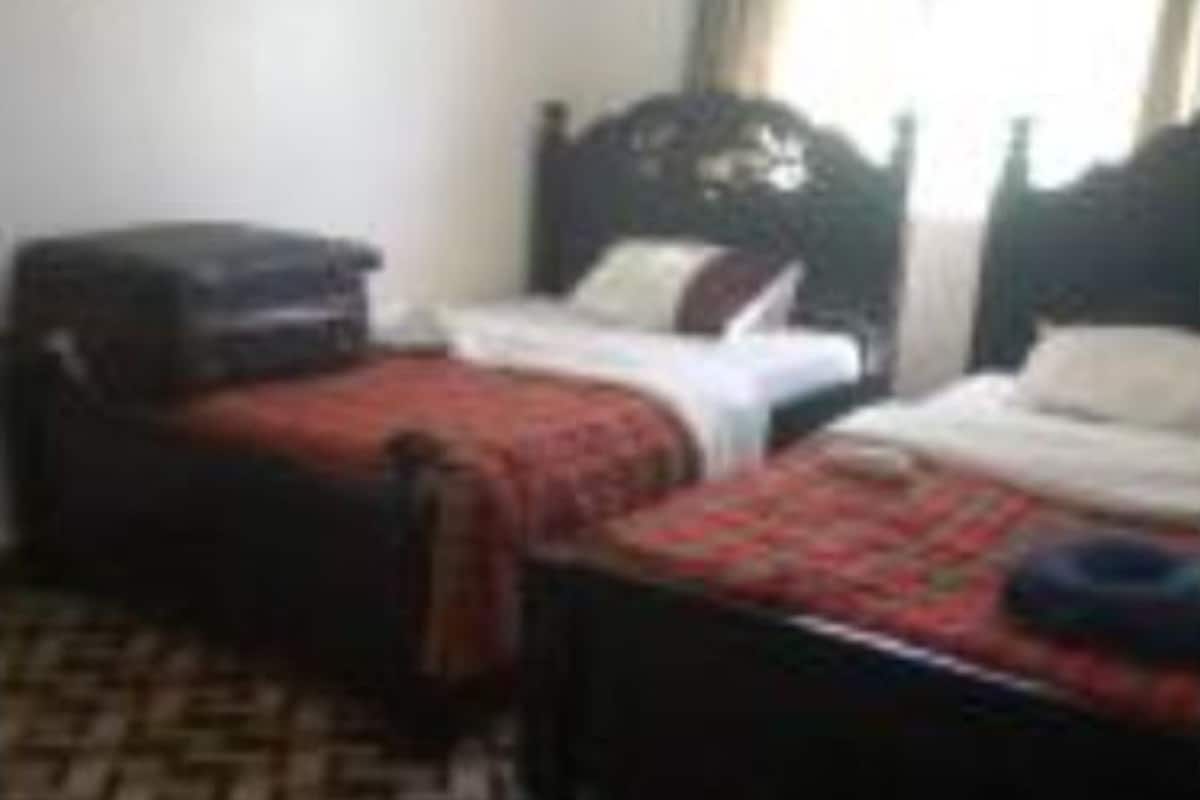 A hotel room with two beds, a patterned carpet, and a window with curtains.
