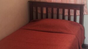 A bed with a red bedspread in a room with a wooden headboard and a plain wall. - Sooper Guest House (Kisumu)