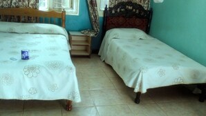A room with two beds, each with a floral-patterned bedspread. There is a wooden headboard on one bed and a red headboard on the other. A small wooden nightstand is between the beds. - Sooper Guest House (Kisumu)
